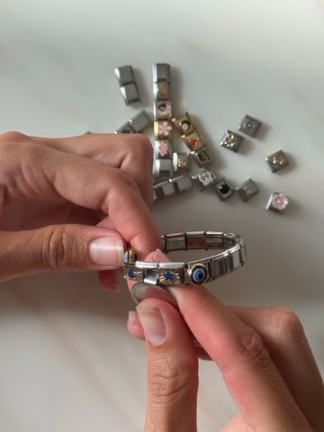 Close up of female hands assembling italian bracelet with multiple charms on the background