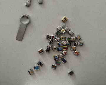 Multiple italian charms and charm tool on white surface