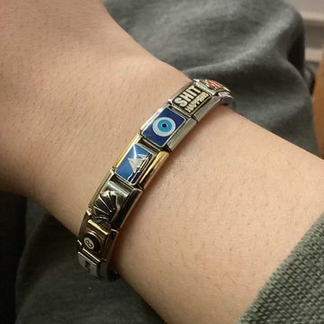 Silver Italian charm bracelet with assorted charms including black 8-ball, silver seashell, paper boat, blue evil eye, and text charm that says "SHIT HAPPENS"