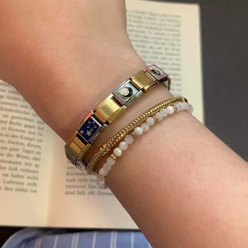 Silver and gold Italian charm bracelet featuring a blue star charm, a diamond-like stone charm, and pink floral detail, worn next to gold and beaded bracelets
